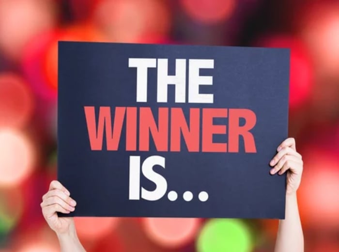 Hands holding up sign for a businesses contest with blurry red background saying The Winner Is